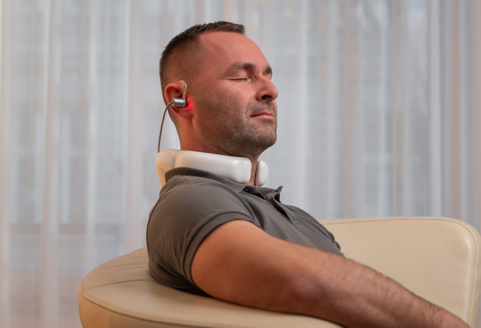 Mann sitzt entspannt im Wohnzimmer und nutzt den LumoHome Laser zur sanften Anwendung am Innenohr.“