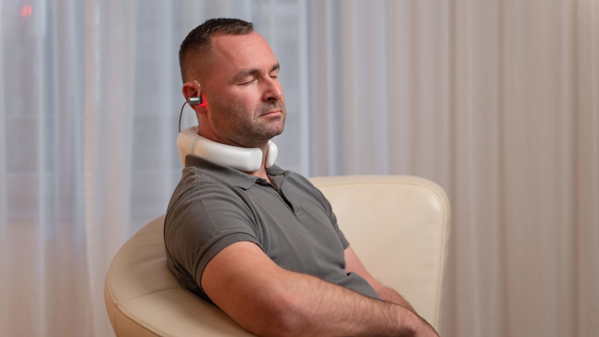 Mann sitzt entspannt im Wohnzimmer und nutzt den LumoHome Laser zur sanften Anwendung am Innenohr.“