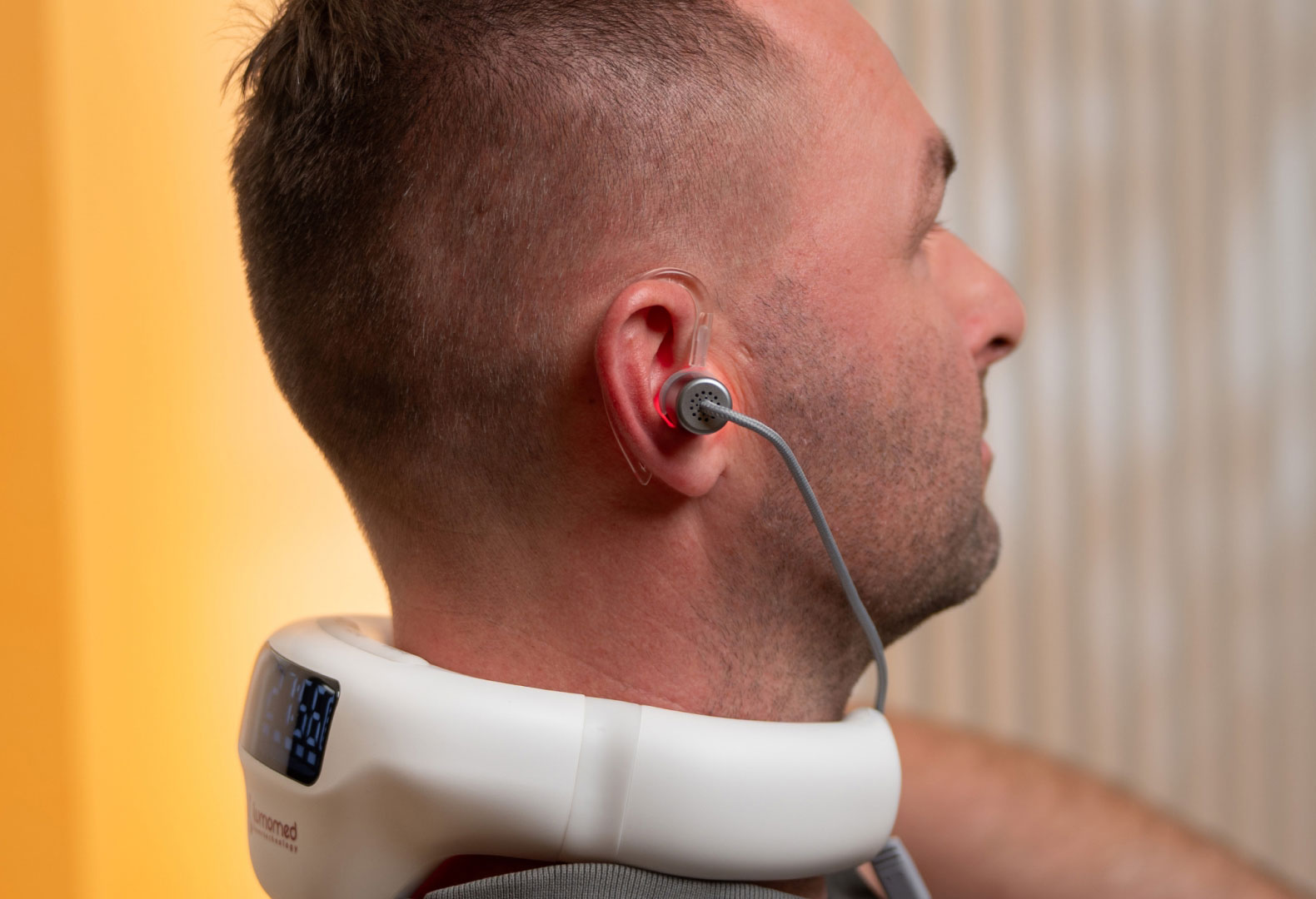 Mann sitzt entspannt im Wohnzimmer und nutzt den LumoHome Laser zur sanften Anwendung am Innenohr.“