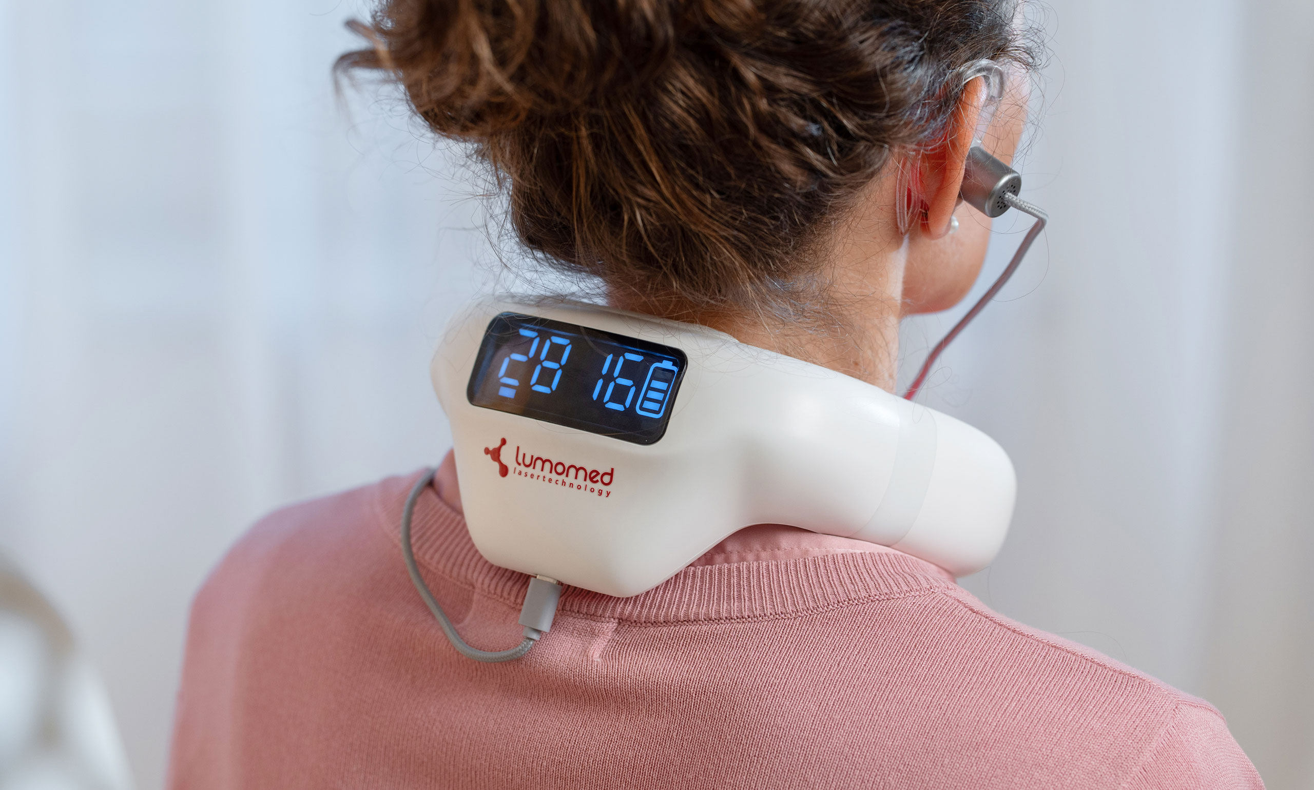 Frau sitzt entspannt im Wohnzimmer und nutzt den LumoHome Laser zur sanften Anwendung am Innenohr.“