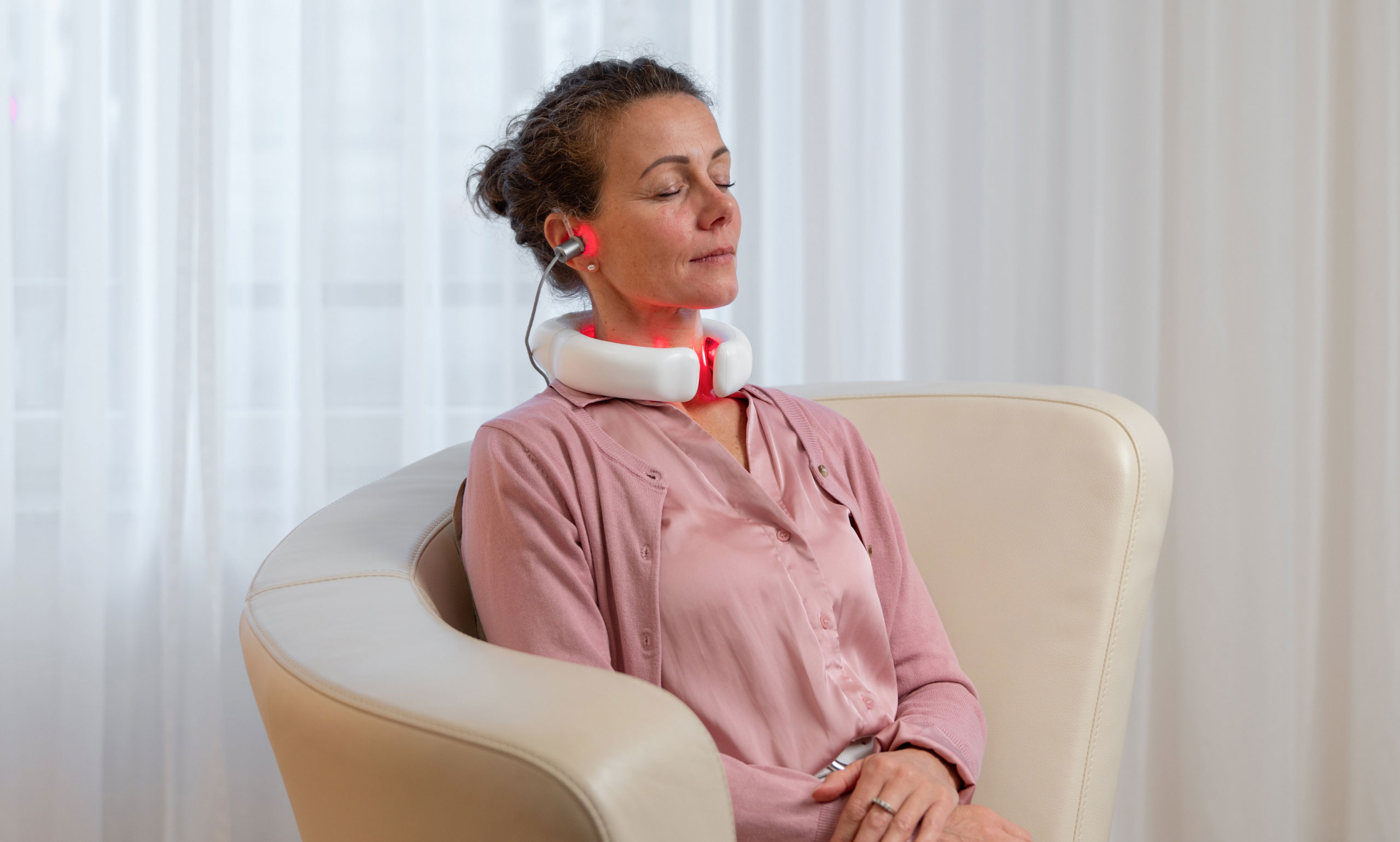 Frau sitzt entspannt im Wohnzimmer und nutzt den LumoHome Laser zur sanften Anwendung am Innenohr.“